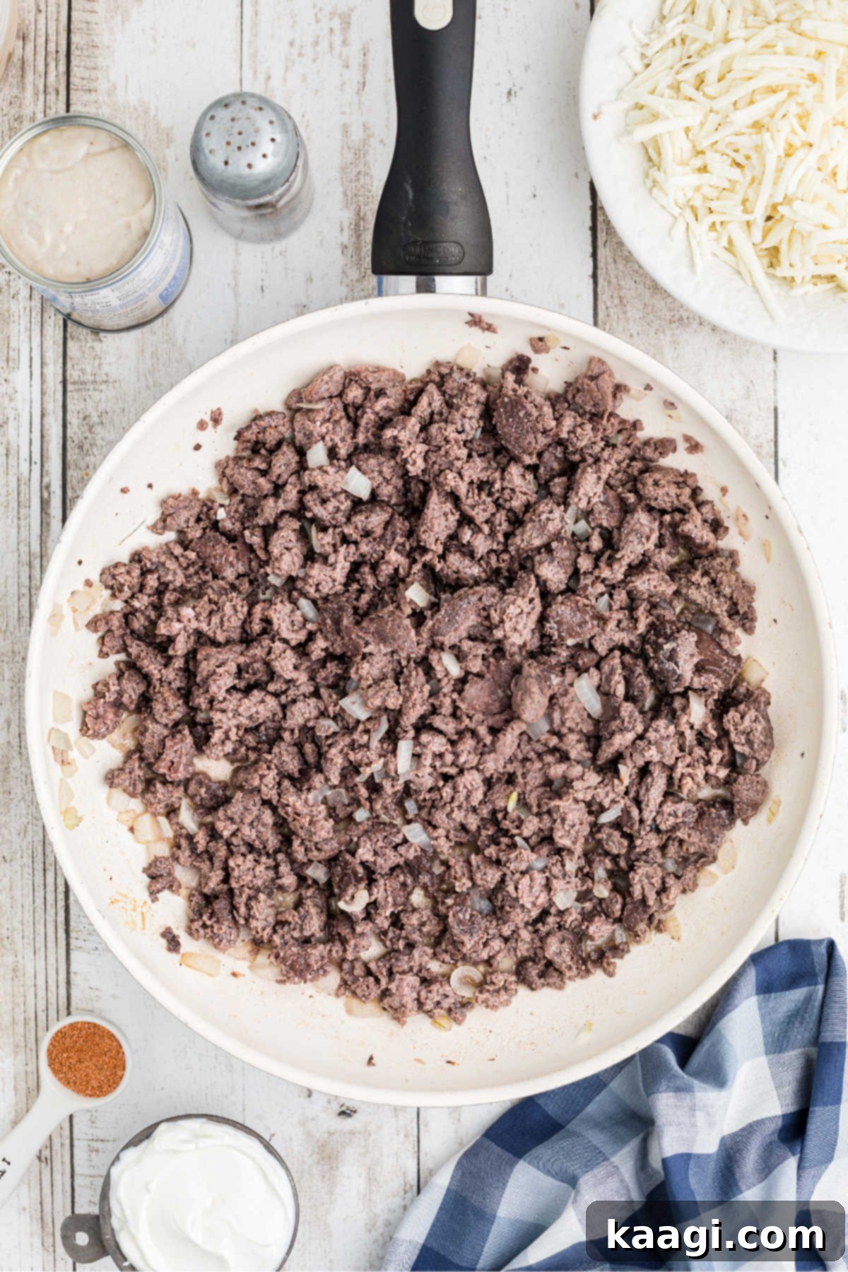 A large skillet with ground beef being cooked until browned, forming a flavorful base for the pinto beans.