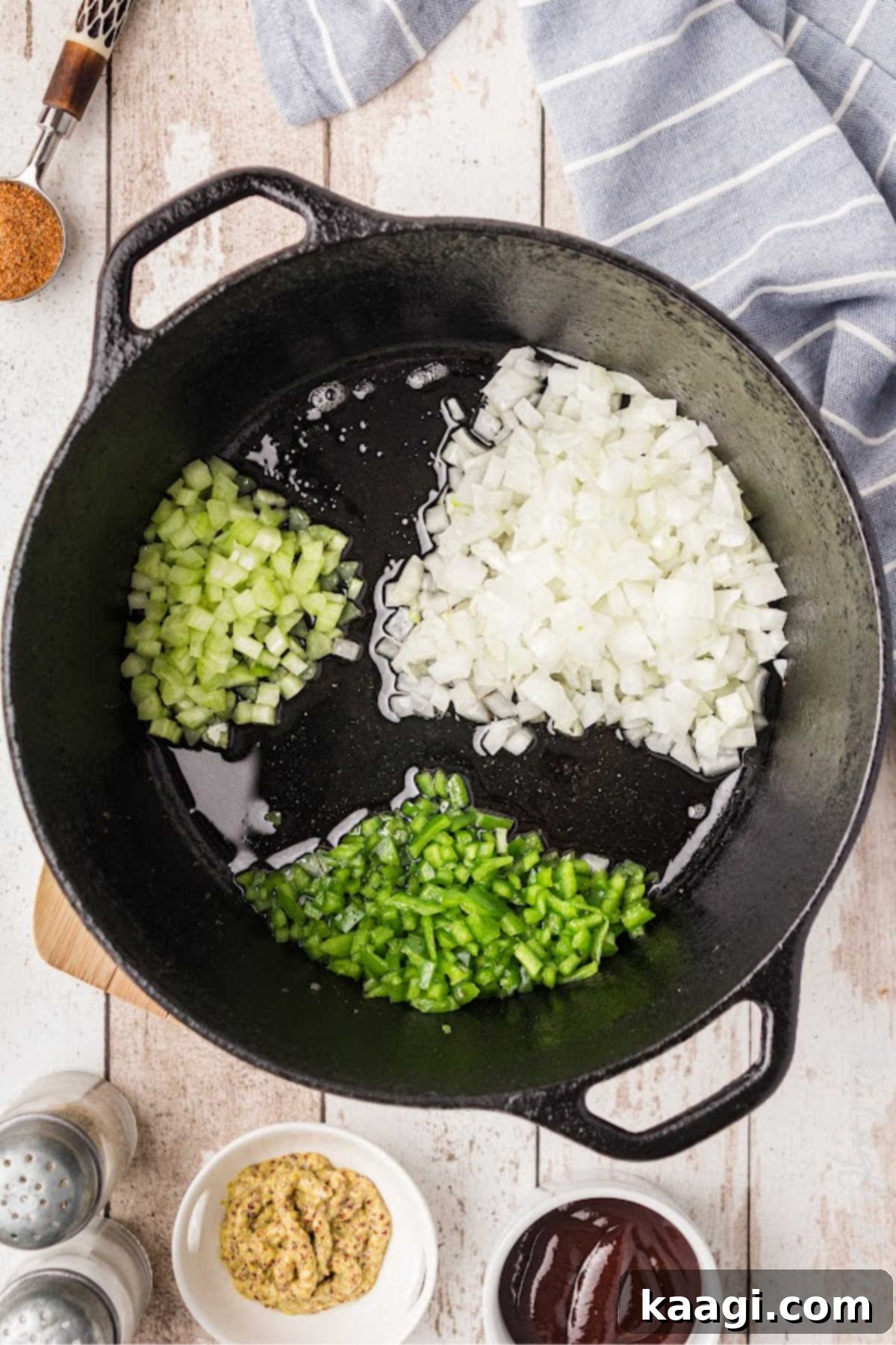 Soulful Southern Baked Beans 5 Onions, bell peppers, and celery, the 'holy trinity,' being added to a cast iron pot with bacon grease, ready to be sautéed until tender.