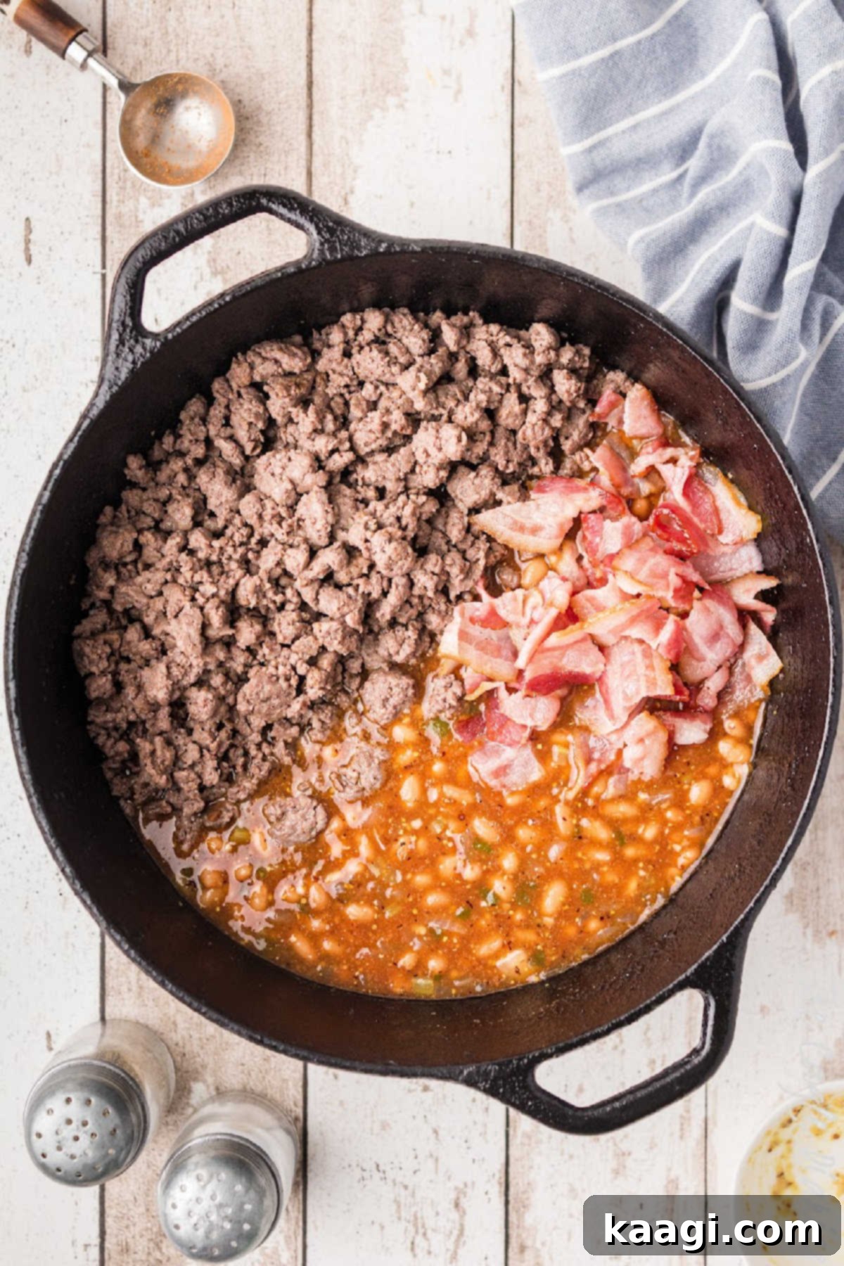 Soulful Southern Baked Beans 7 A cast iron pot of Southern Baked Beans, topped with crispy bacon pieces, simmering slowly to allow flavors to meld and deepen.