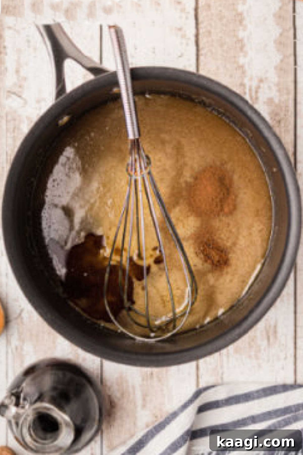 A wire whisk actively mixing vanilla extract, nutmeg, and cinnamon into the slightly cooled sugar and butter mixture, ensuring thorough incorporation.