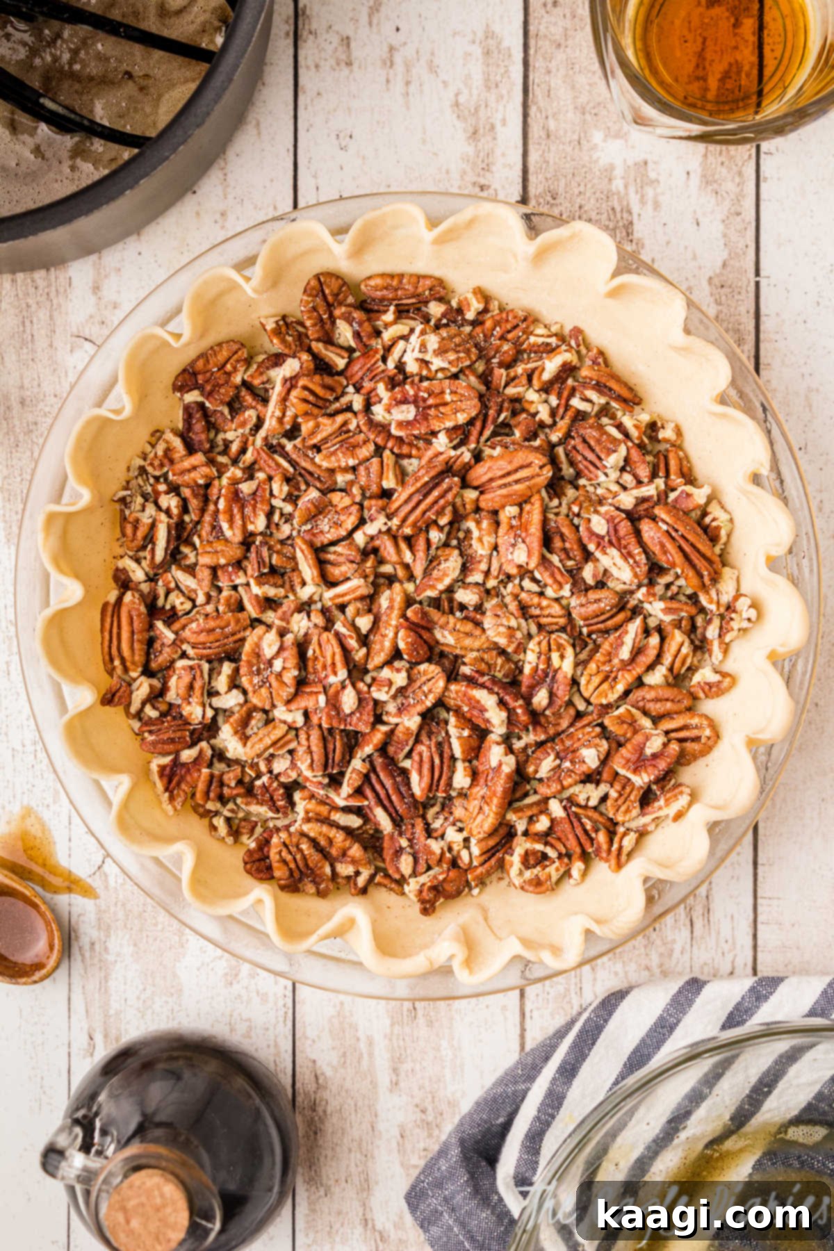 A generous layer of chopped pecans evenly distributed across the bottom of a prepared pie crust, awaiting the pour of the filling.