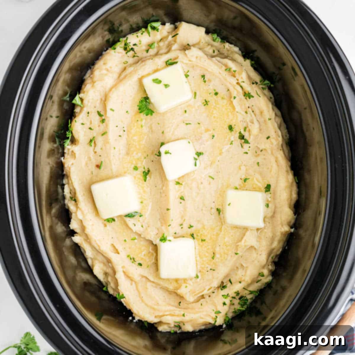 Overhead image of slow cooker mashed potatoes, made with chicken broth and garnished with pats of butter, for enhanced flavor.