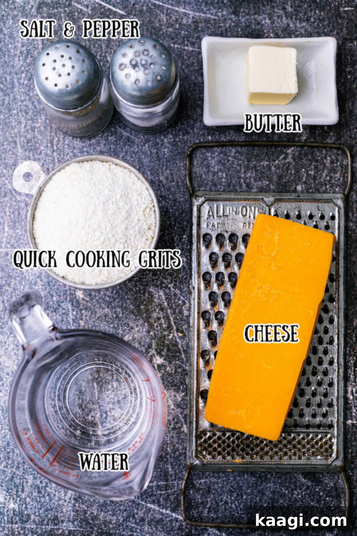 A rustic wooden surface displaying the key ingredients required for making cheese grits: a bowl of yellow grits, a block of cheddar cheese, a stick of butter, salt, and black pepper.