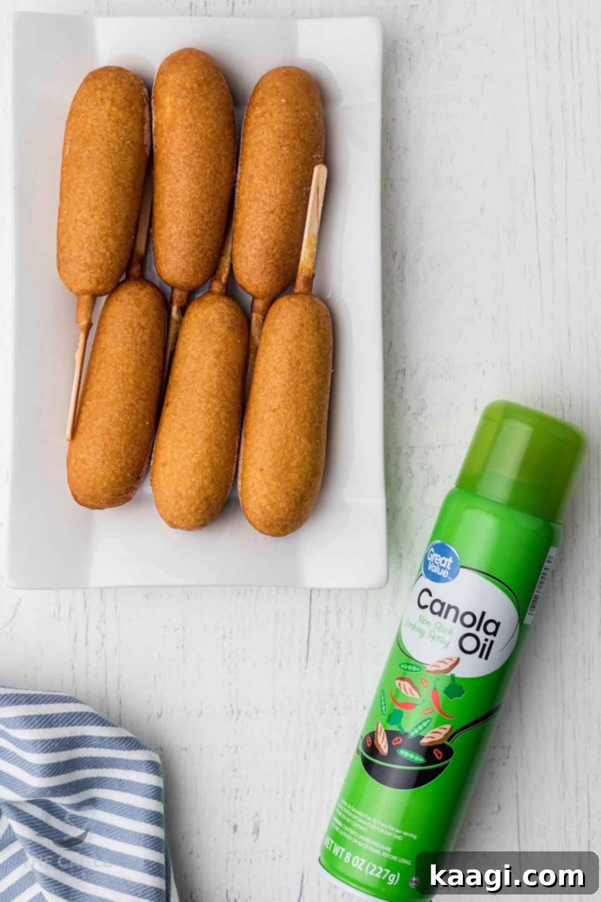 A neatly arranged plate of crispy corn dogs, accompanied by a can of canola oil cooking spray, ready for serving.