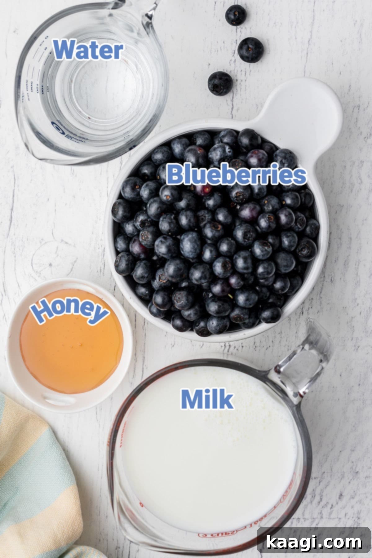 Velvet Berry Elixir 3 A flat lay photograph showcasing fresh blueberries, a jar of honey, a glass of water, and a bottle of milk, all laid out as ingredients for blueberry milk.