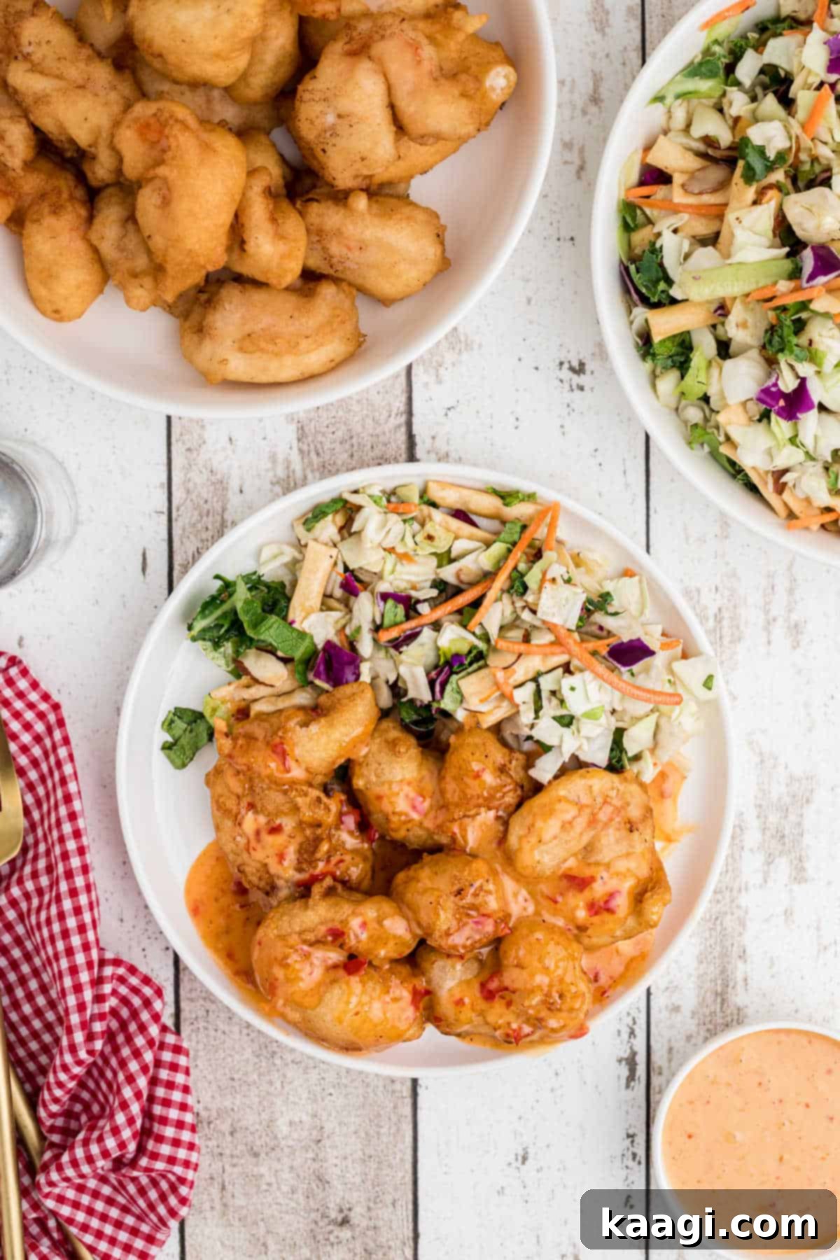 Plate full of perfectly battered and fried shrimp drizzled generously with a sweet and spicy boom boom sauce, served with a fresh green salad in the background.
