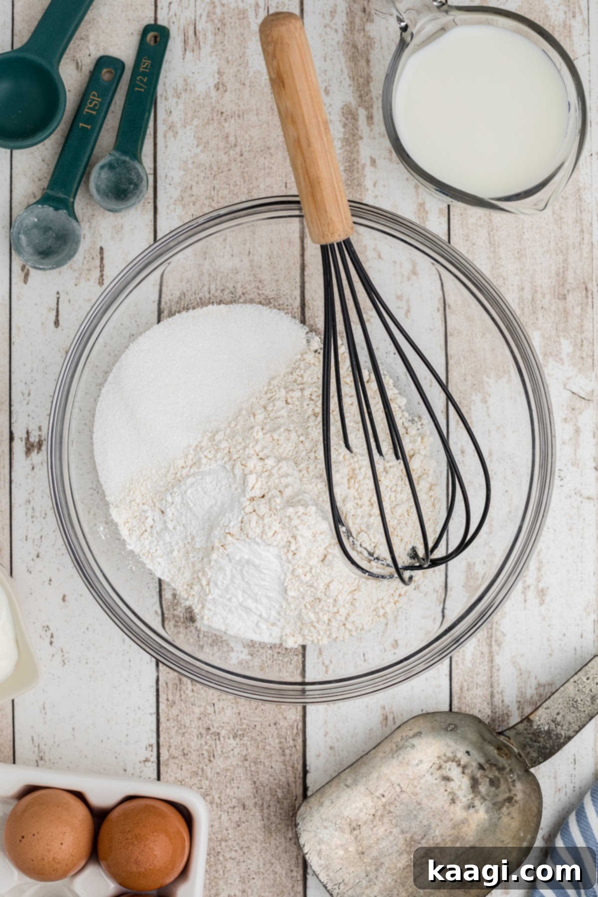 A large mixing bowl with flour and other ingredients with a whisk.