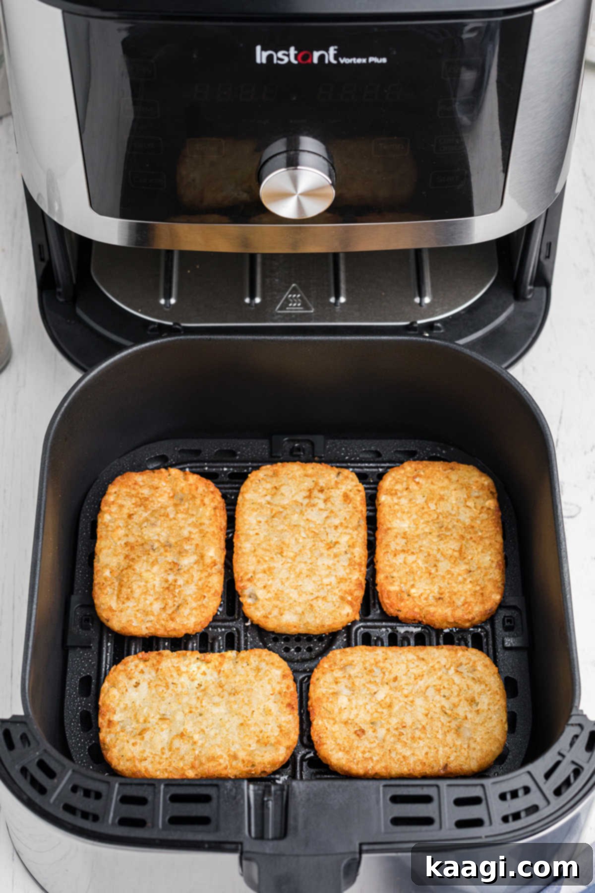 An open air fryer showing 5 golden-brown hash browns cooked to perfection
