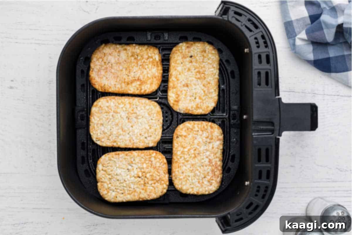 An air fryer basket with frozen hash browns lined up, ready to be cooked