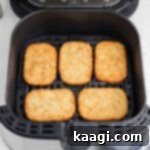 An air fryer basket with 5 hash brown patties lined up