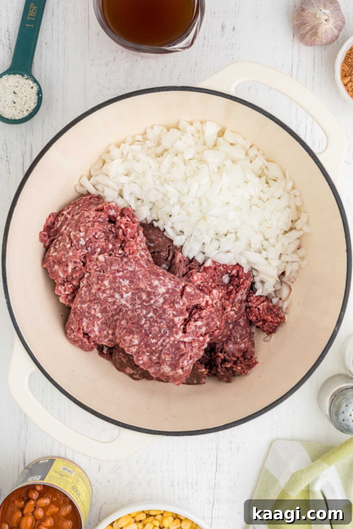 A large Dutch oven pot with some onions and ground beef browning.