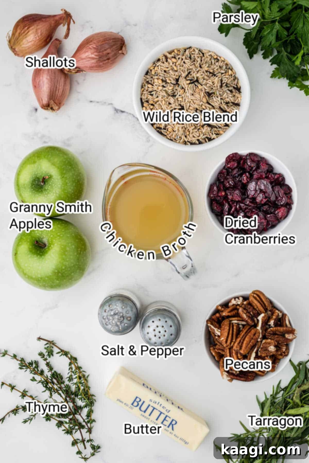 Ingredients for a cranberry apple rice pilaf spread out on a kitchen surface with labels, including rice mix, broth, butter, shallots, apples, cranberries, pecans, and fresh herbs.