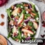 A bowl of salad with apples and red onions and cranberries with a spoon on the side