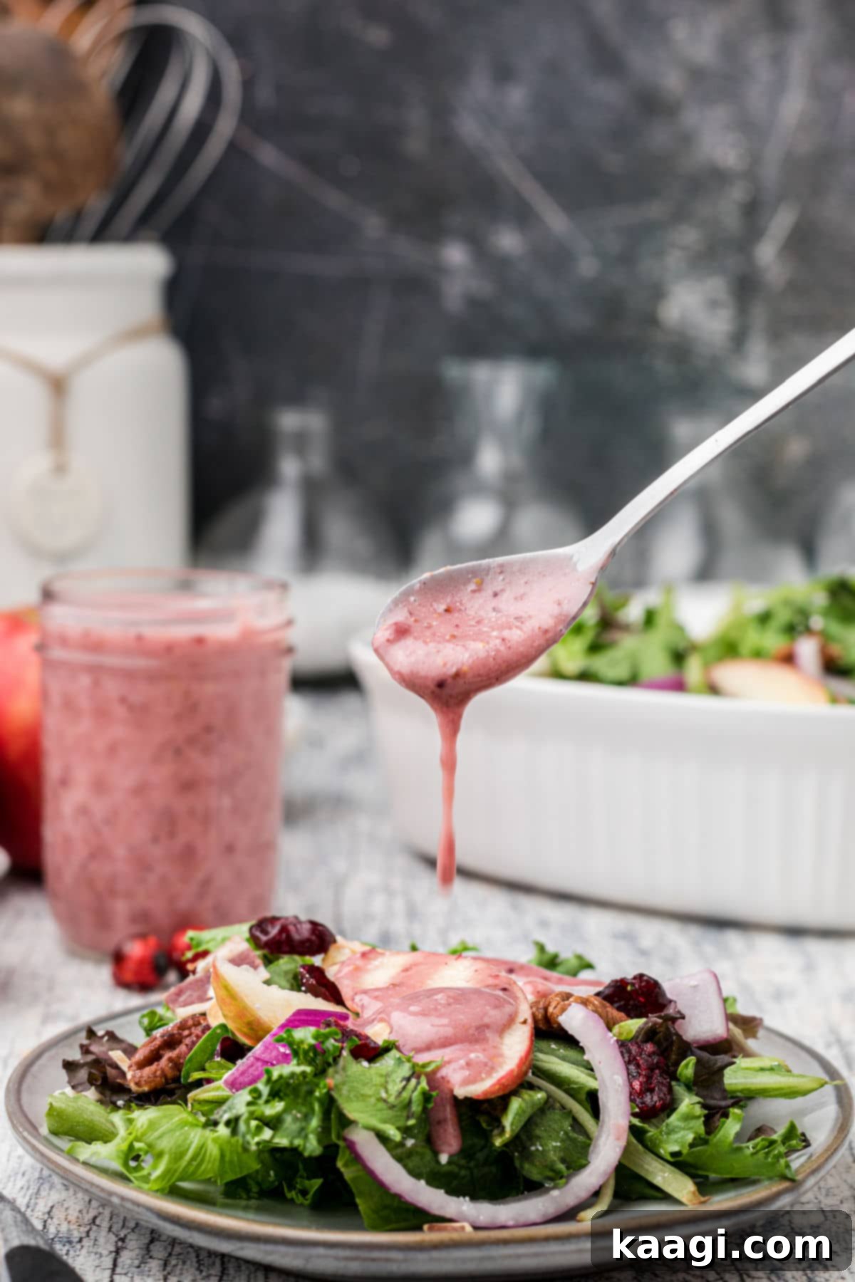 Crimson Vinaigrette 2 A spoon generously dripping homemade cranberry vinaigrette over a fresh, vibrant salad, highlighting the dressing's beautiful color and inviting texture. Perfect for fall and winter salads.