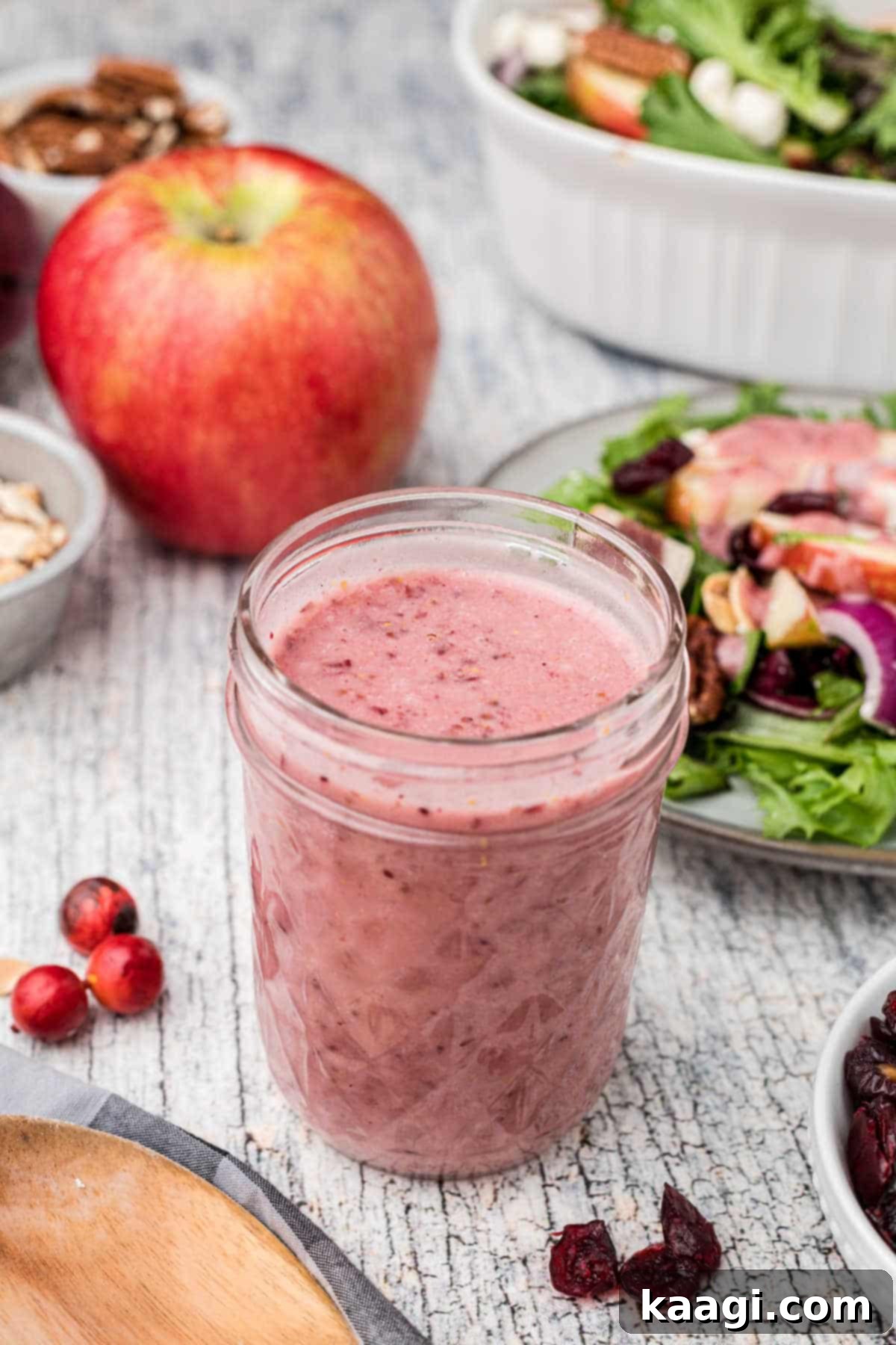 Crimson Vinaigrette 5 A charming glass jar of freshly made cranberry vinaigrette, positioned in front of a blurred background of a fresh salad and scattered cranberries, emphasizing its delightful appeal.