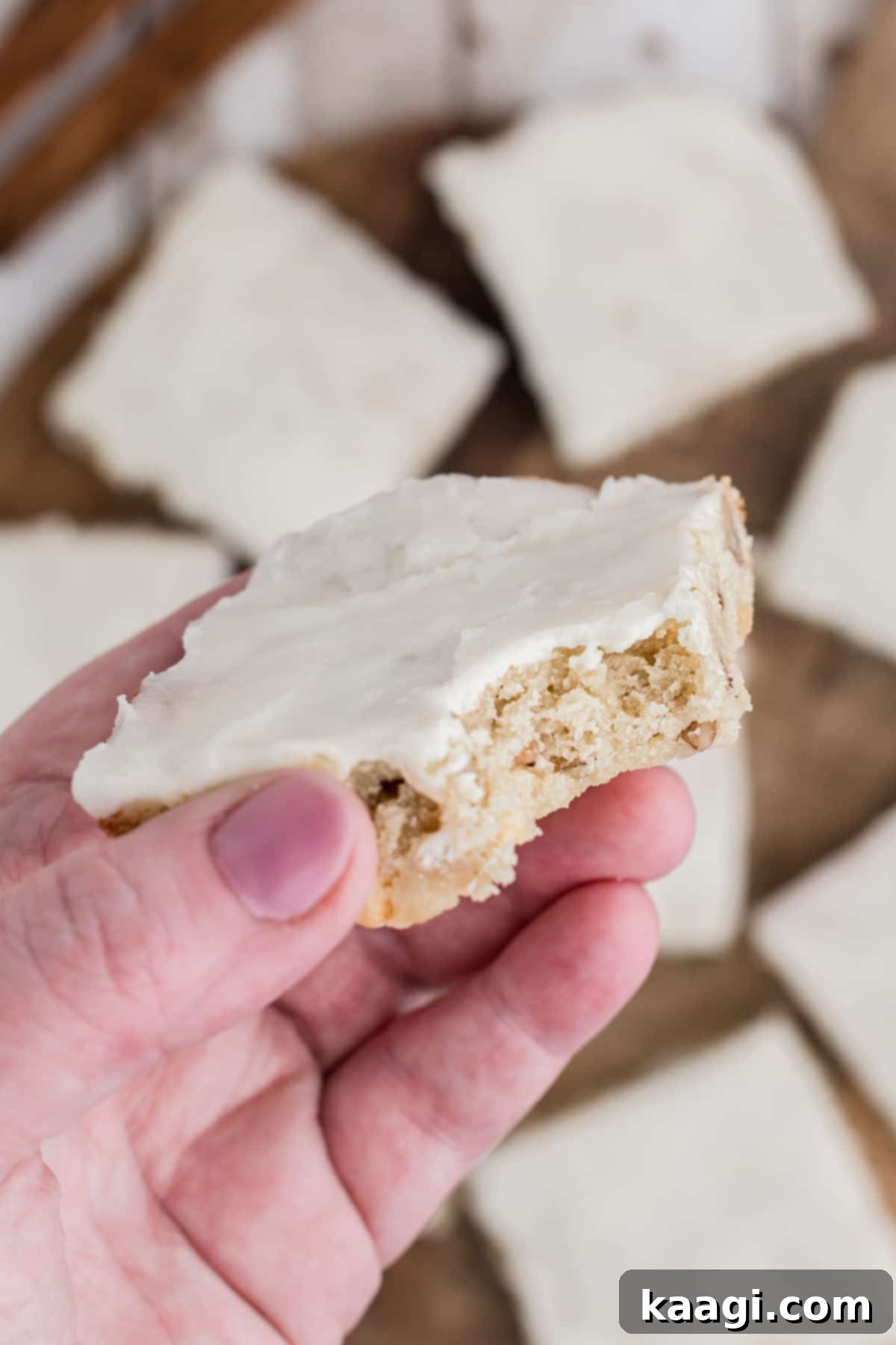A close up of a hand holding a vanilla brownie with a bite taken out of it, showing its fudgy interior