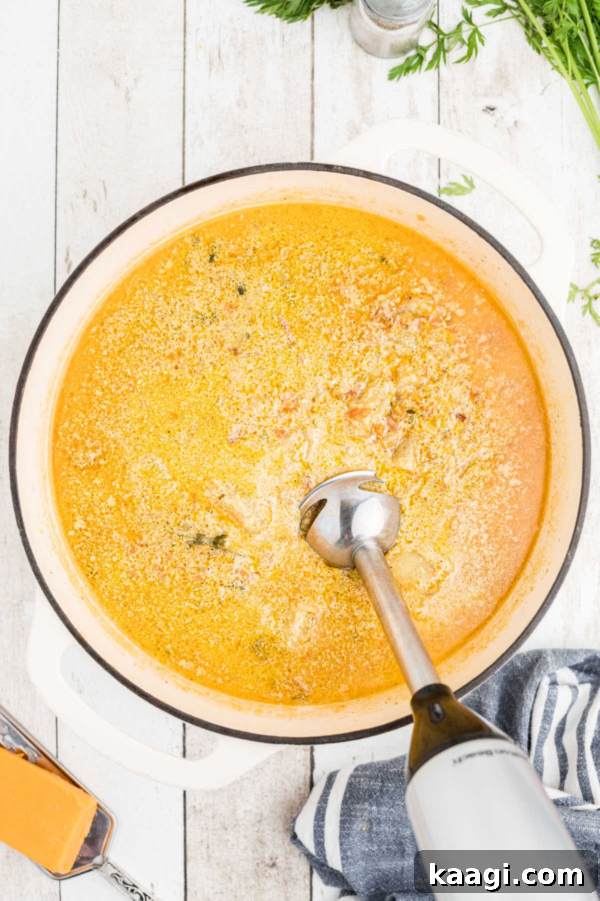 A stick blender actively being used to blend the cooked potato soup directly in the Dutch oven, creating a smooth and creamy texture.