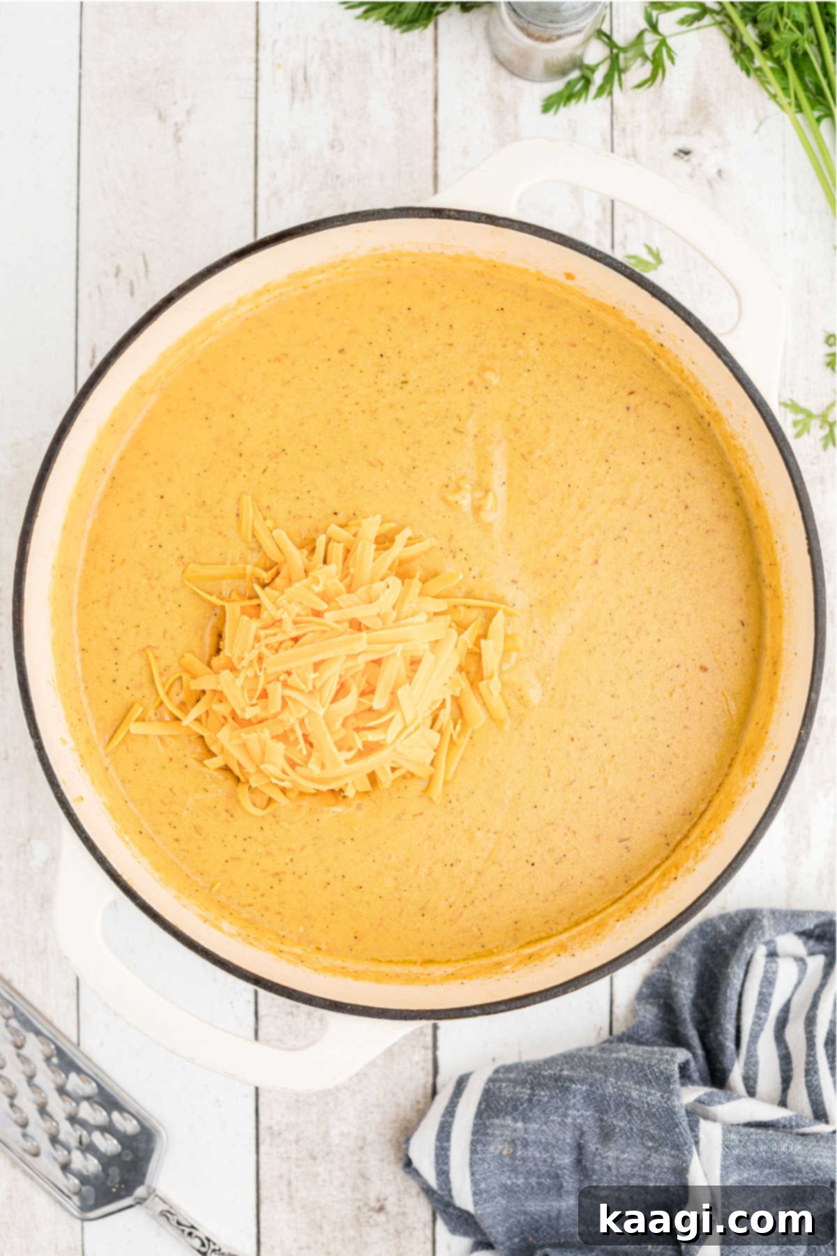 Grated cheddar cheese being stirred into the hot, creamy potato soup in a large pot, melting and integrating into the rich mixture.