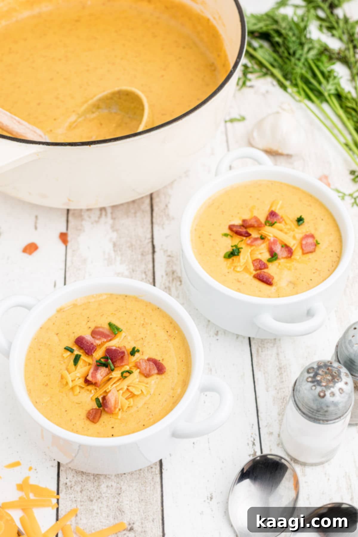 A side view of two steaming bowls of Saltgrass baked potato soup, perfectly garnished, with the large pot in the soft-focused background, ready for serving.