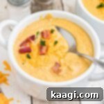 Close-up picture of a bowl of creamy Saltgrass baked potato soup, garnished with crispy bacon and melted cheese, with a spoon ready to dive in.