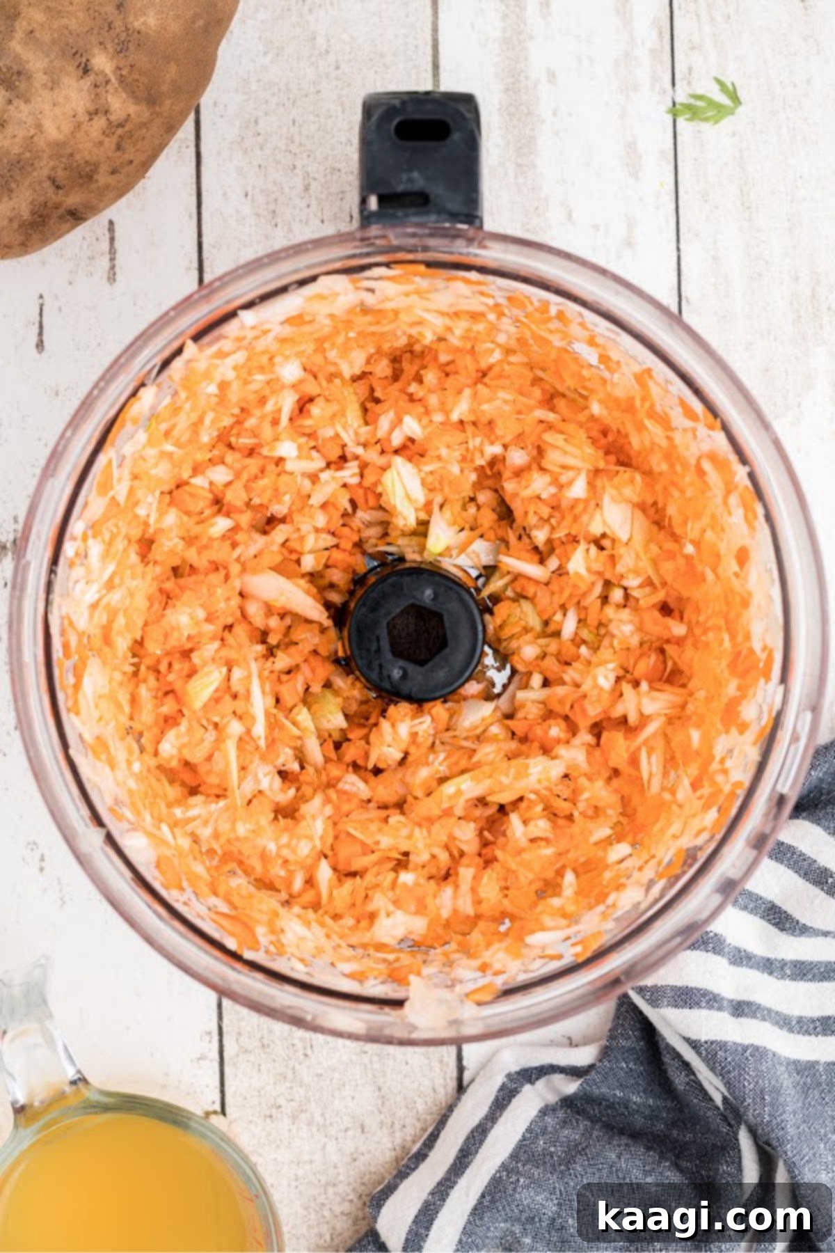 A close-up shot of vibrant carrots, onions, and celery being finely chopped in a food processor, demonstrating preparation for the soup base.