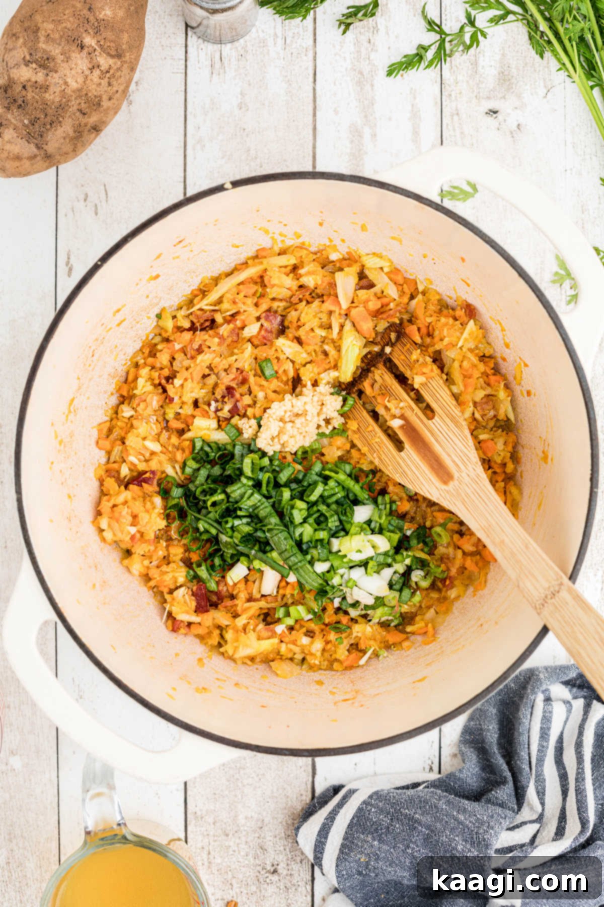 Chopped green onions and minced garlic being added to the sautéed vegetables in the large pot, ready to infuse their fresh aromas into the soup base.