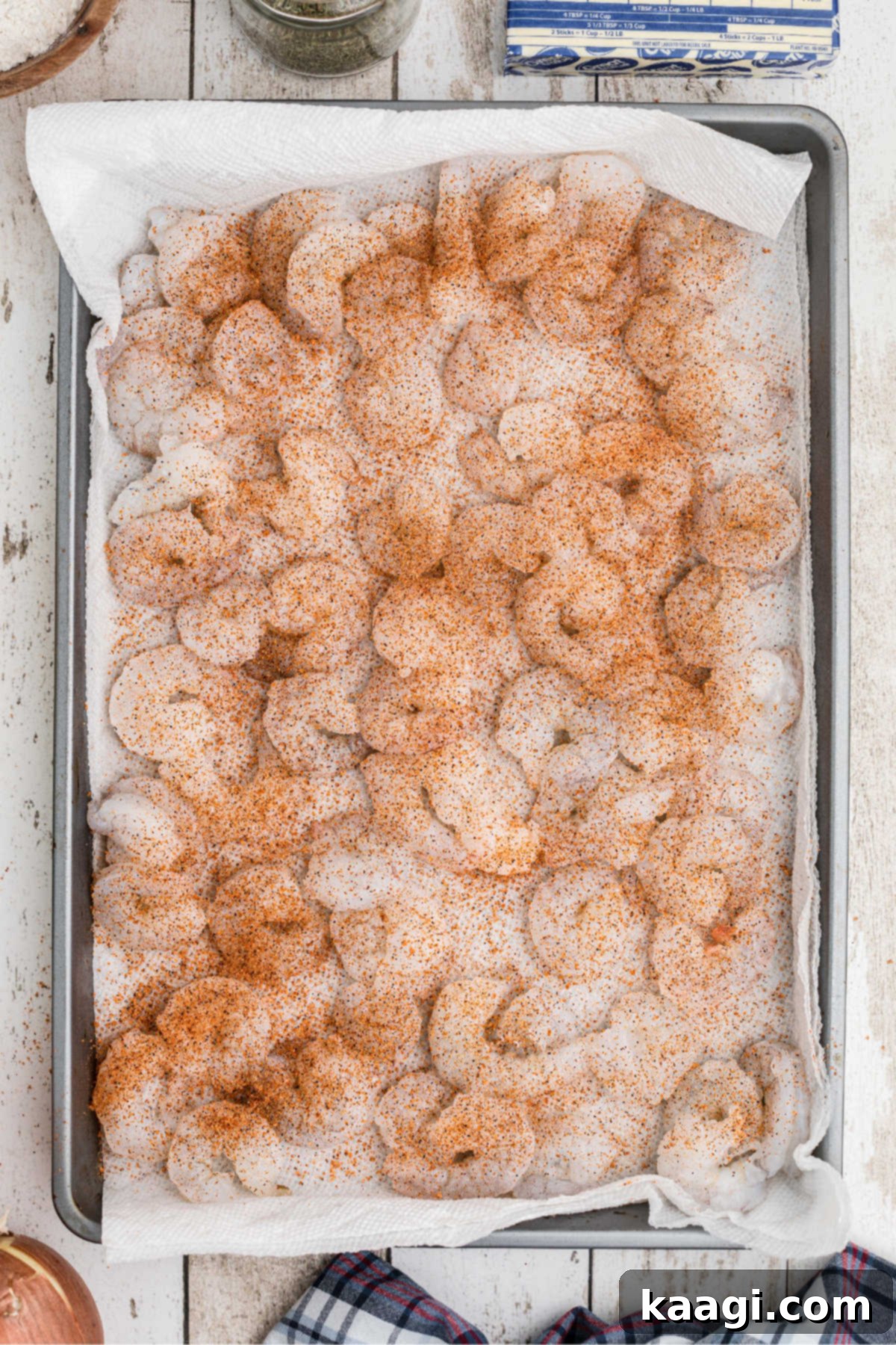 A baking sheet lined with paper towel and shrimp on top soaking in seasoning.