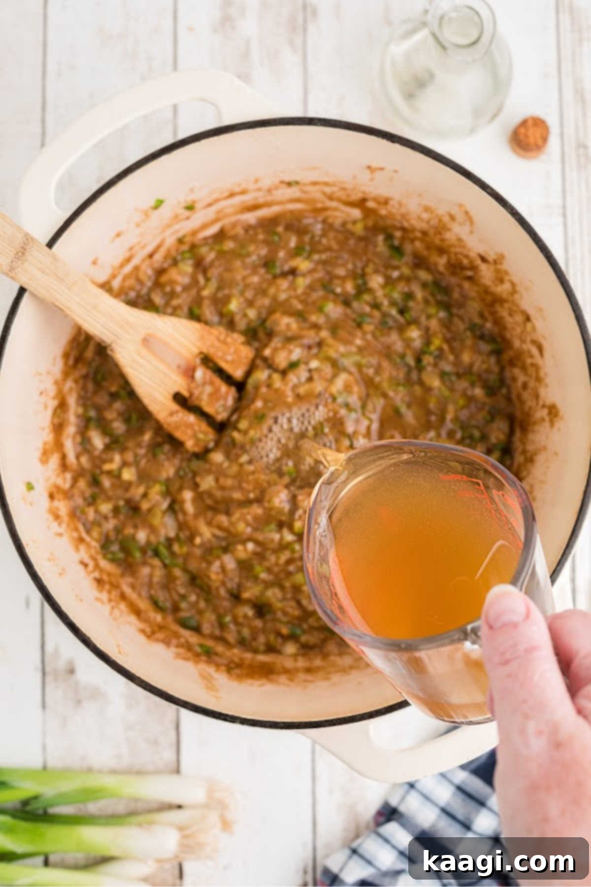Broth being added to a large Dutch oven that's cooking etouffee.