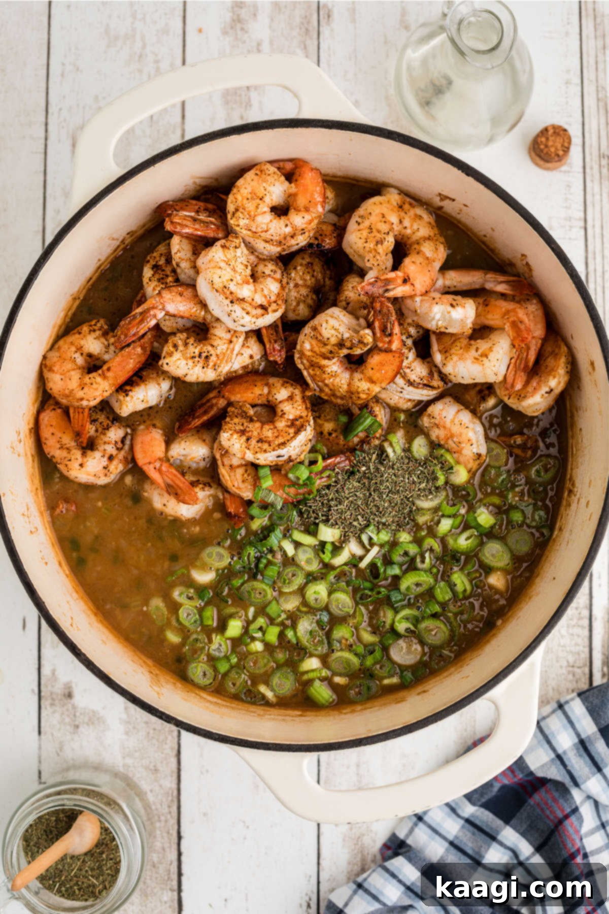 Shrimp and seasonings being added to a large Dutch oven with etouffee in it.