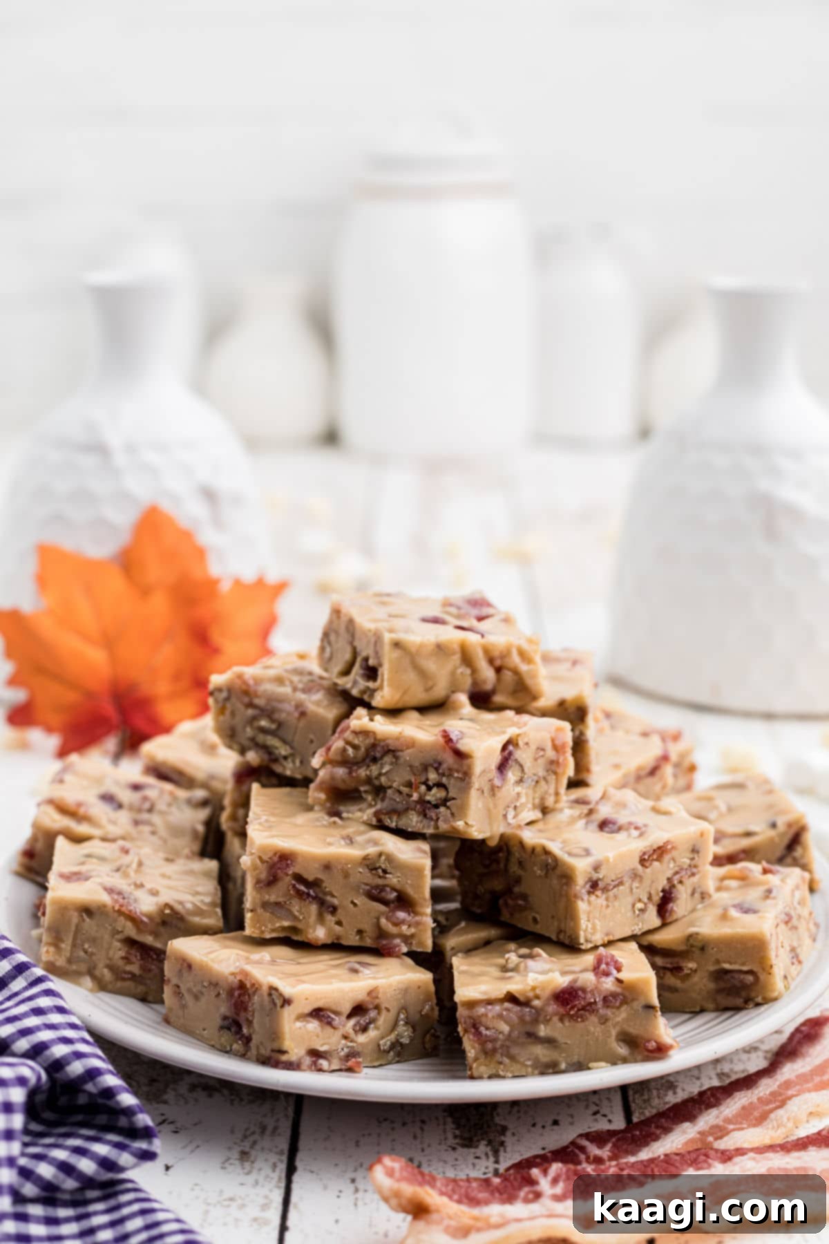 A plate full of maple bacon fudge squares, with a maple leaf in the background and some bacon slices for garnish.