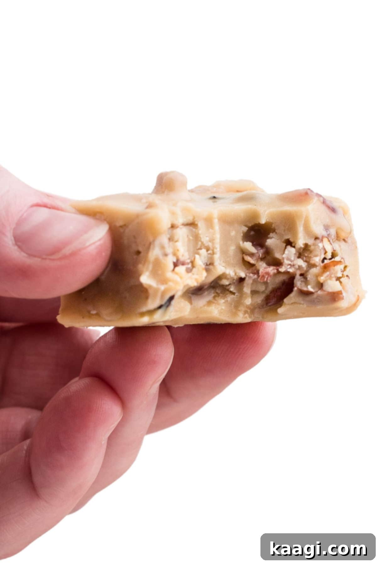 A hand holding a piece of maple bacon fudge with a bite taken out, showcasing its texture.