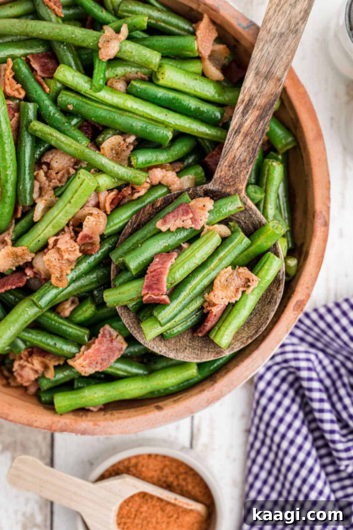 A close-up shot of a bowl brimming with perfectly cooked Cajun Green Beans and crispy bacon bits, with a serving spoon poised to scoop a generous portion.