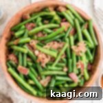 A close-up of a ceramic bowl full of Cajun Green Beans with crispy bacon bits, ready to be served and enjoyed.