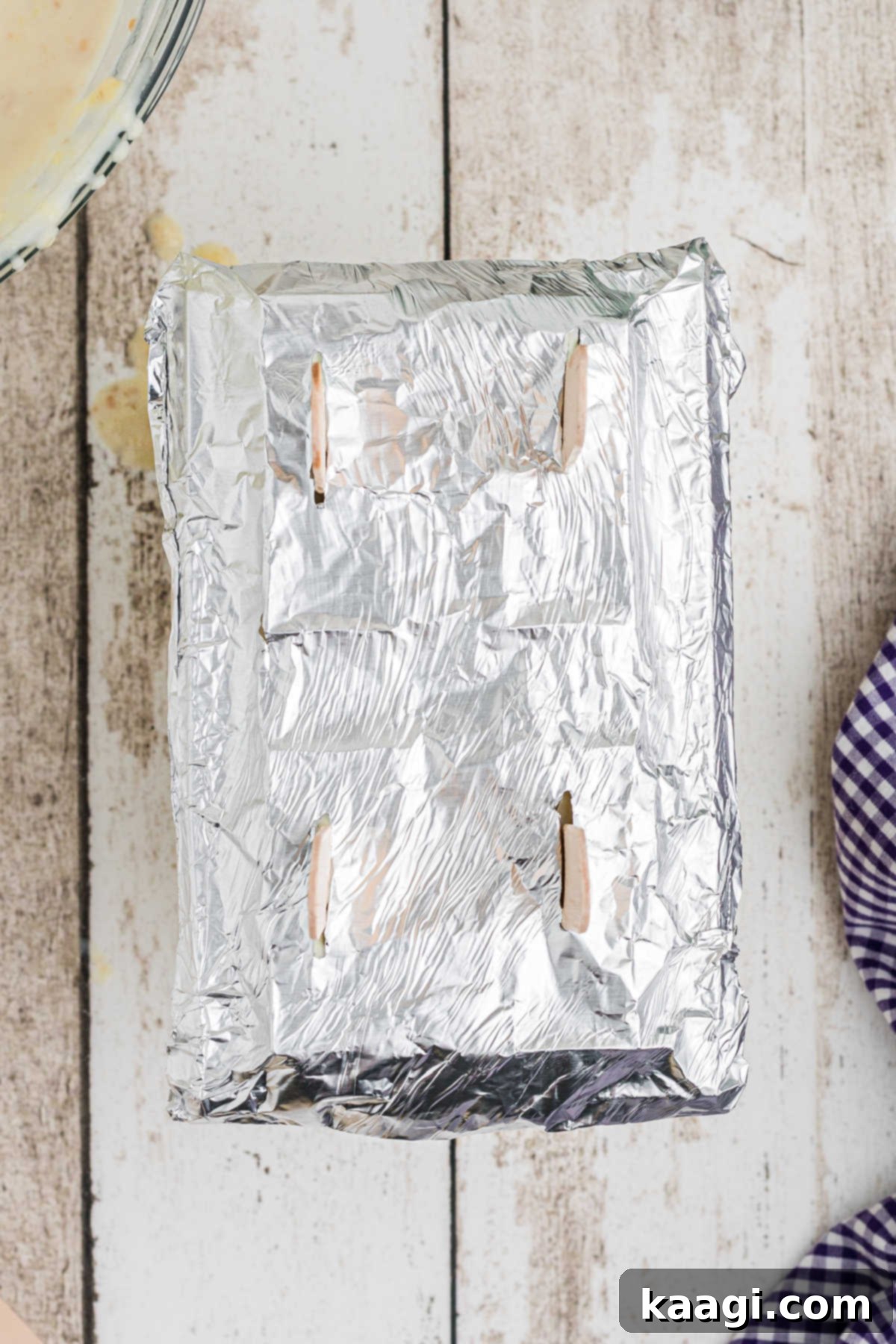 A popsicle mold covered with foil, with popsicle sticks protruding through slits, ready for freezing.