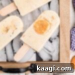 Close up of a tray with ice and several banana pudding popsicles resting on top, garnished with banana slices and vanilla wafers.