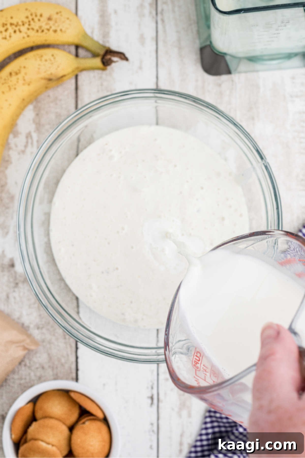 The mashed banana and yogurt mixture in a bowl, with half-and-half being poured in for added creaminess.