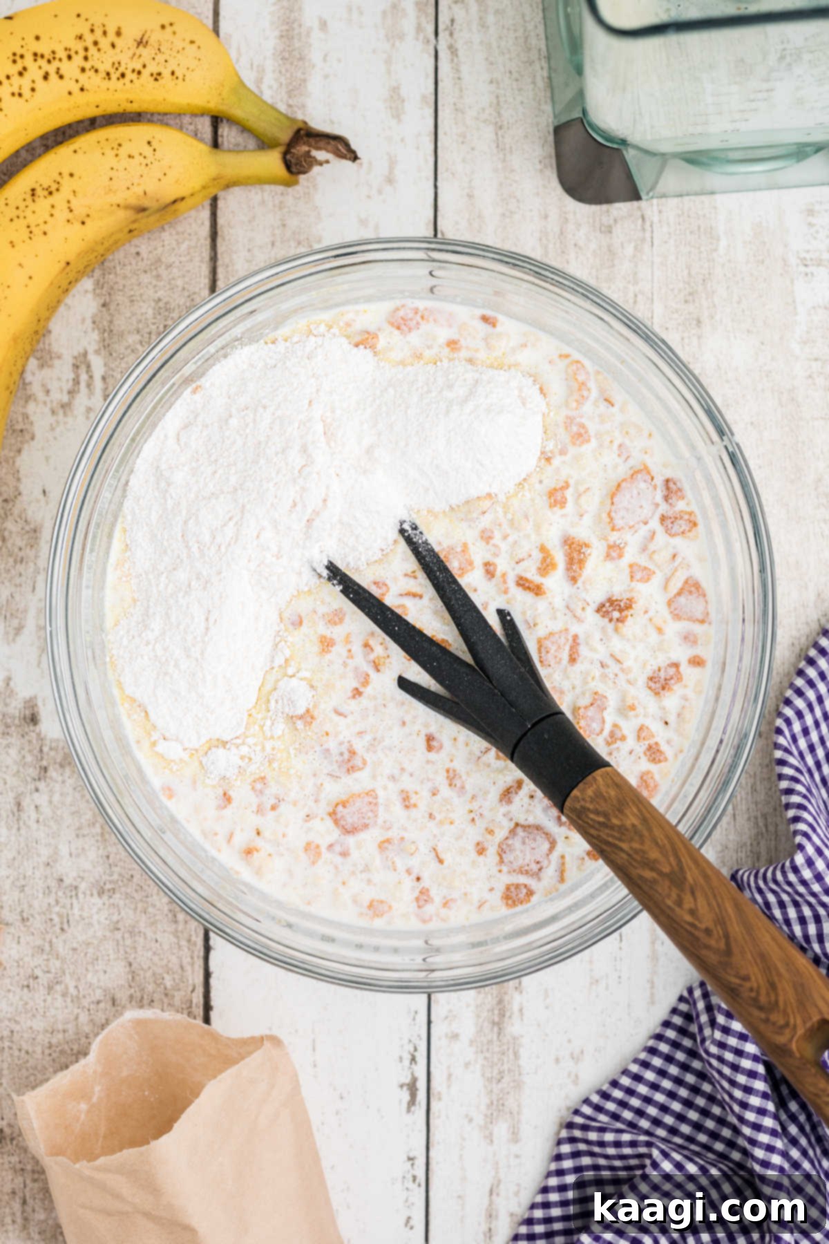 A packet of vanilla pudding mix being poured into the mixing bowl with the banana, cream, and crushed cookie mixture.