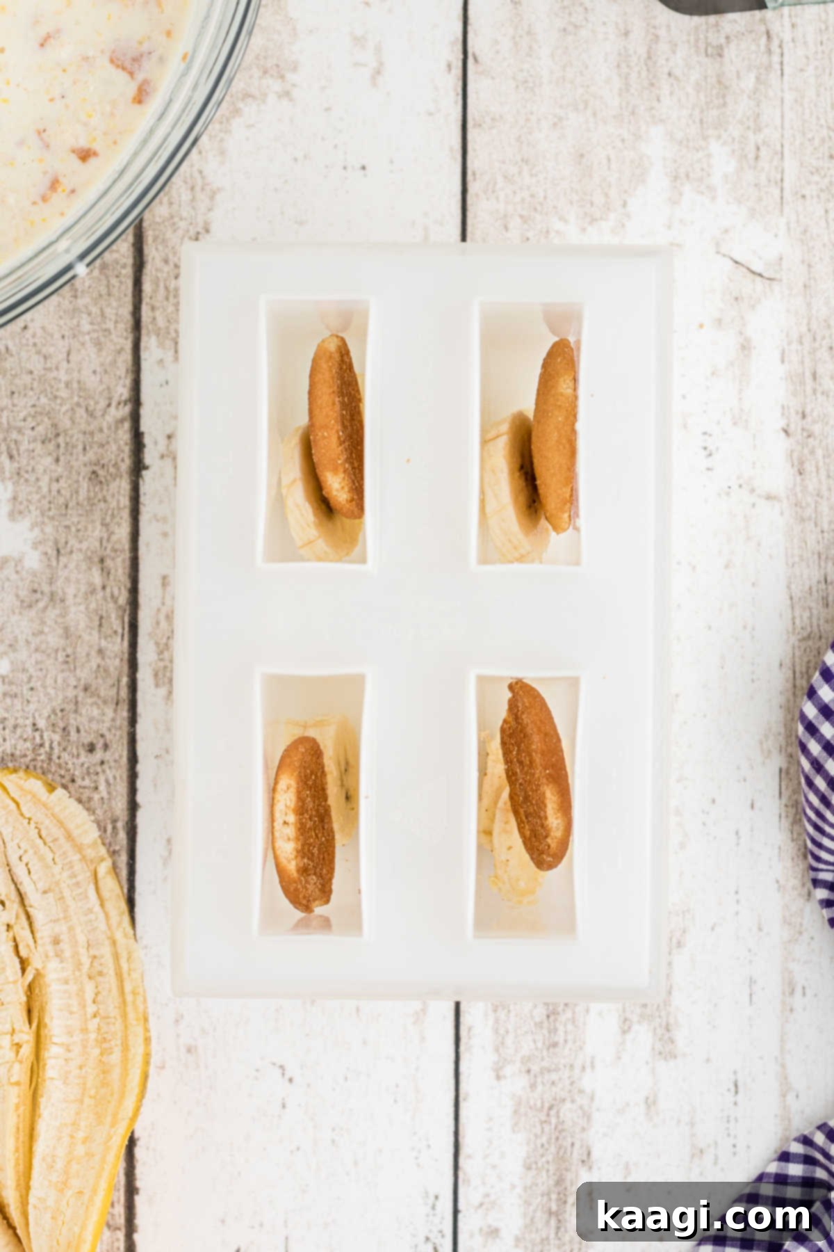 Slices of fresh banana and whole vanilla wafers being carefully placed into the individual compartments of a popsicle mold.