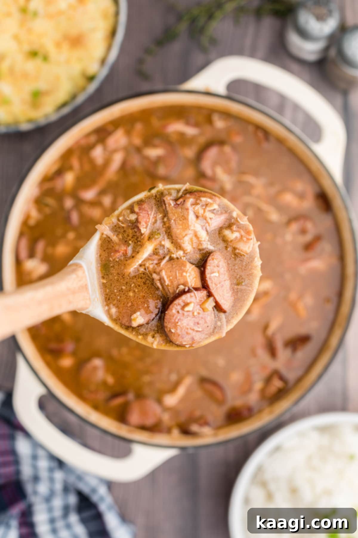 a ladle of chicken and sausage gumbo held up to the camera with the pot of gumbo beneath