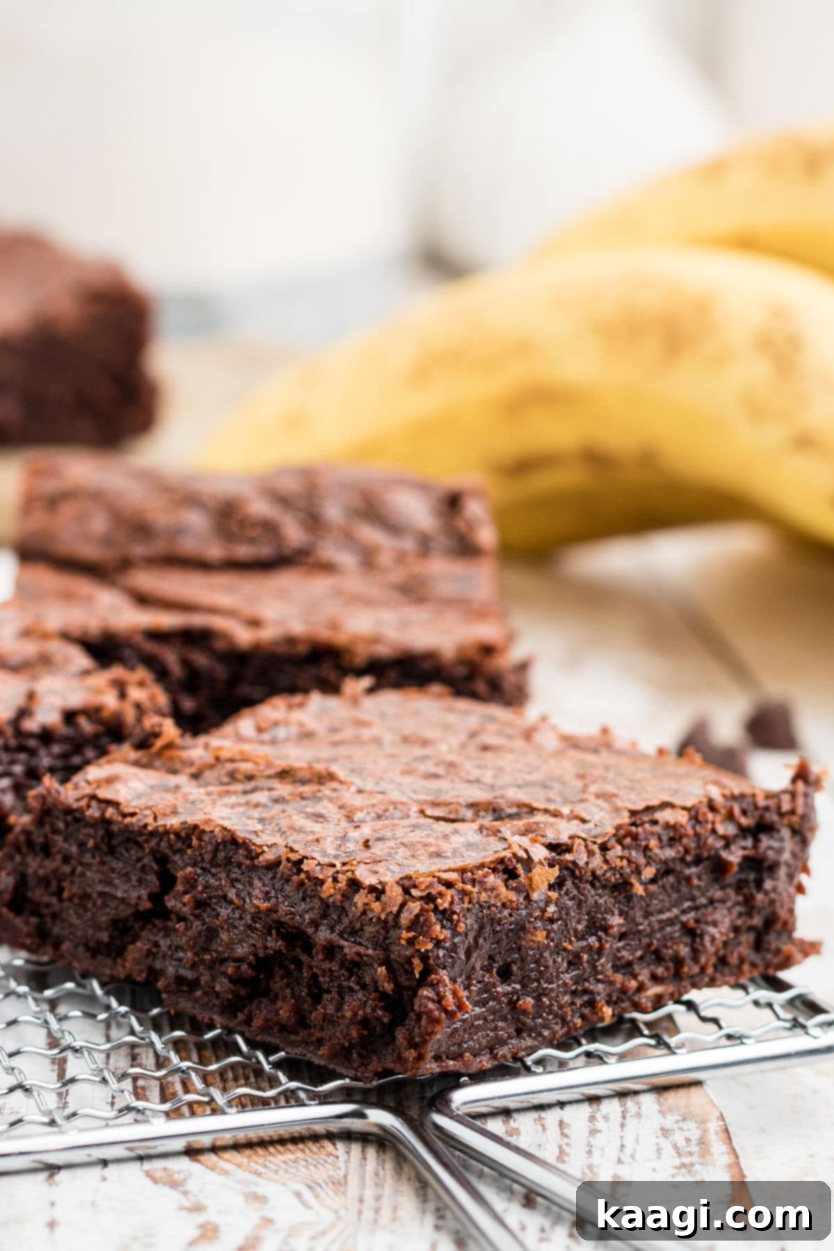 Decadent Banana Brownies 2 A close-up of a moist banana brownie with fresh bananas in the soft background, highlighting its rich chocolate color and fudgy texture.