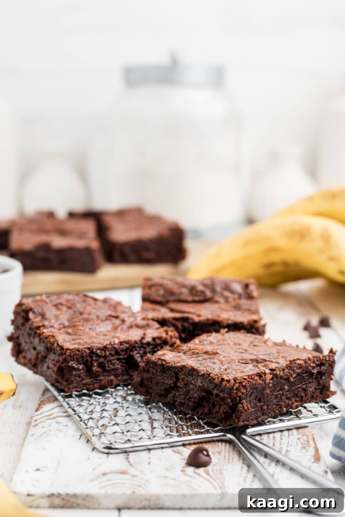 Decadent Banana Brownies 8 A small, elegant wire rack holding three beautifully baked banana brownies, with a subtle blur of fresh bananas in the background, suggesting their key ingredient.