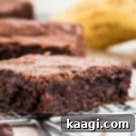 Decadent Banana Brownies 10 A close-up of a moist banana brownie with a ripe banana in the soft background, emphasizing its rich texture and banana flavor.
