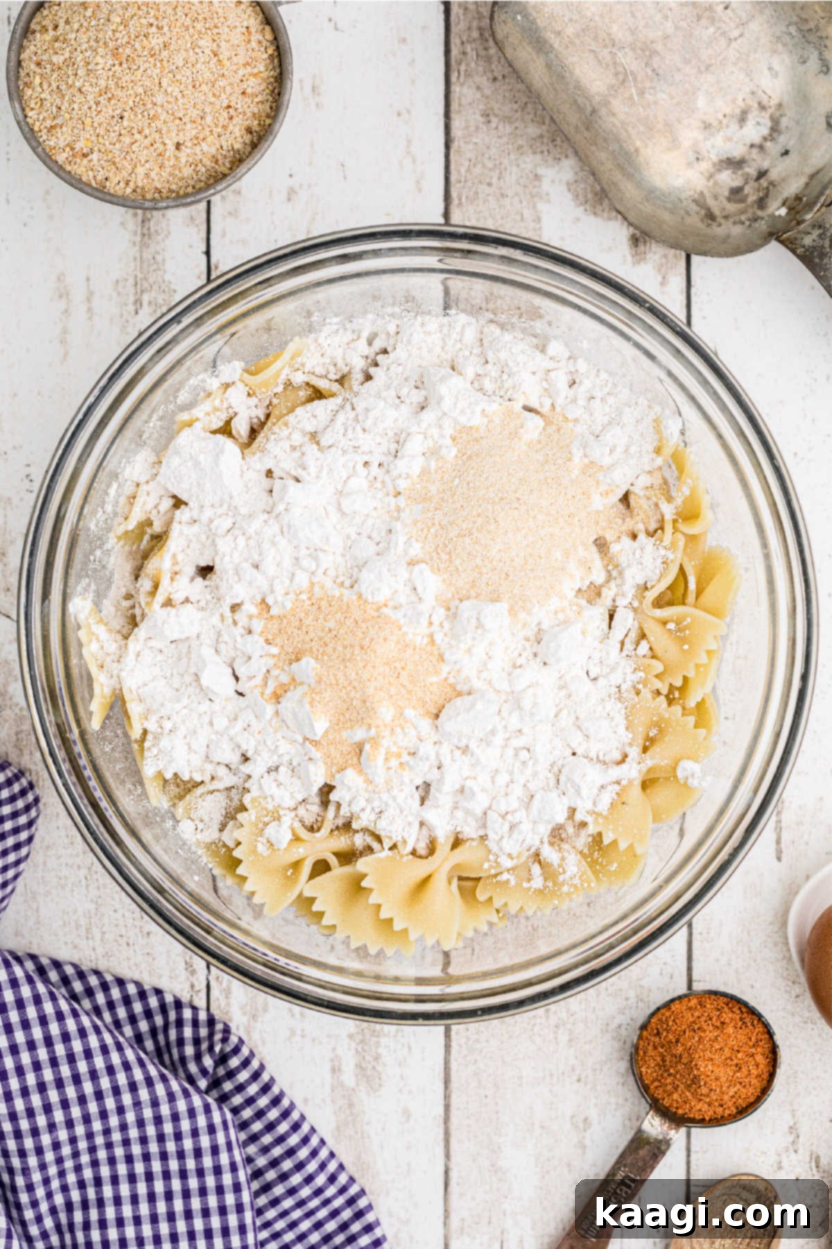 Crispy Farfalle Bites 6 A large mixing bowl containing cooked and dried bowtie pasta, with all-purpose flour, onion powder, and garlic powder added, ready for mixing.