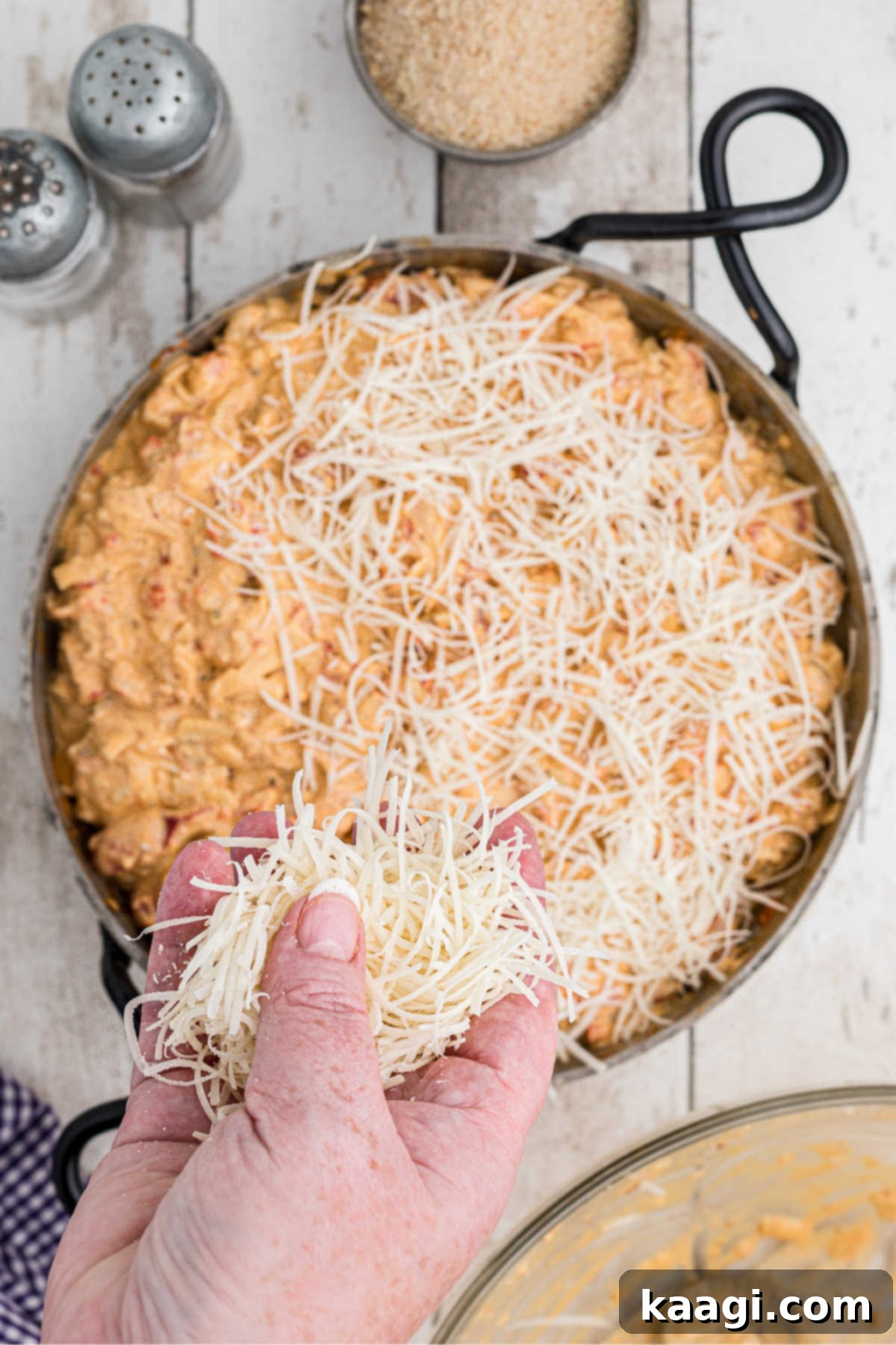 A cheesy crawfish mixture in a skillet being topped with cheese.