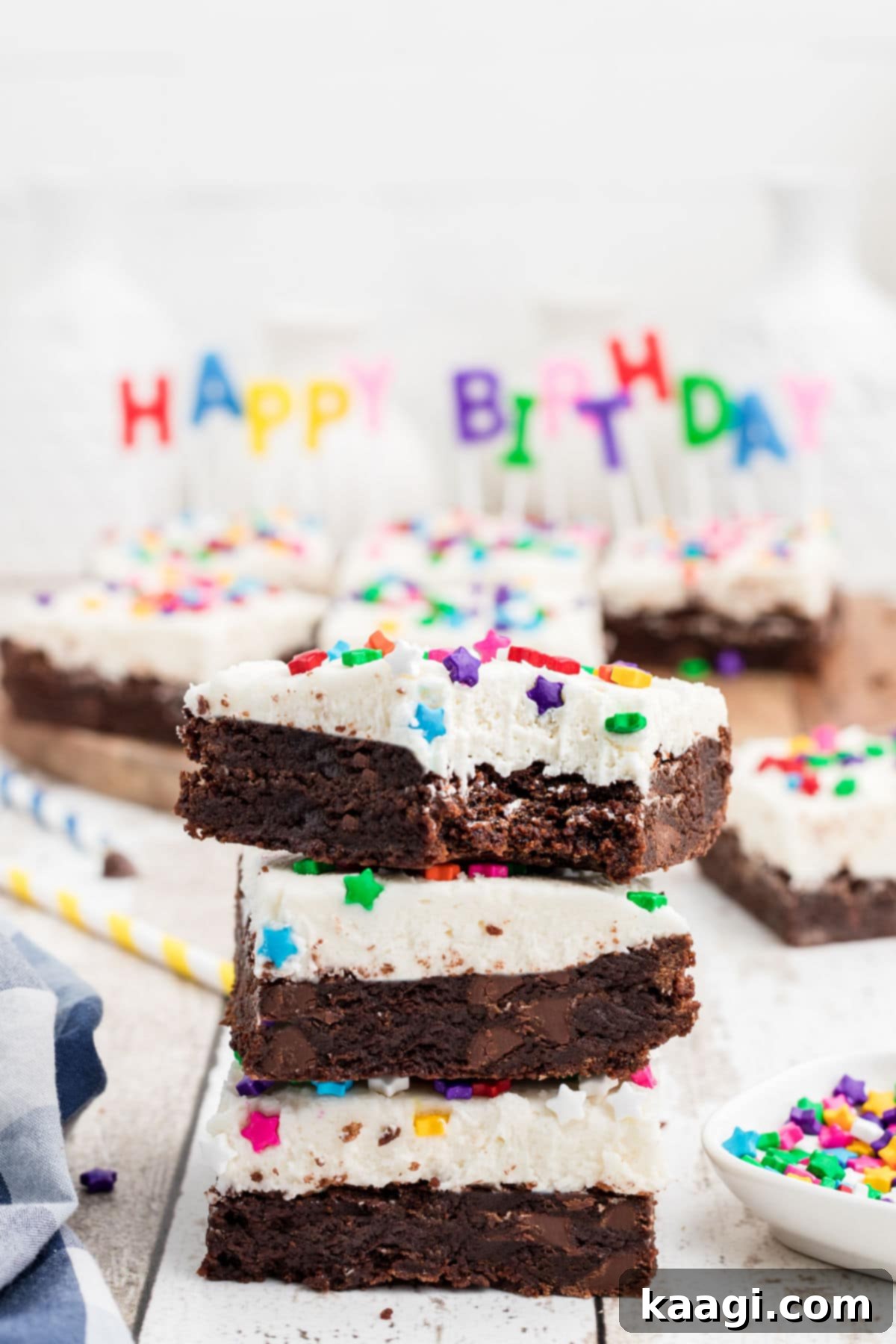 A close-up view of a stack of celebratory birthday brownies, one with a delectable bite taken out, set against a cheerful 'Happy Birthday' banner in the background.