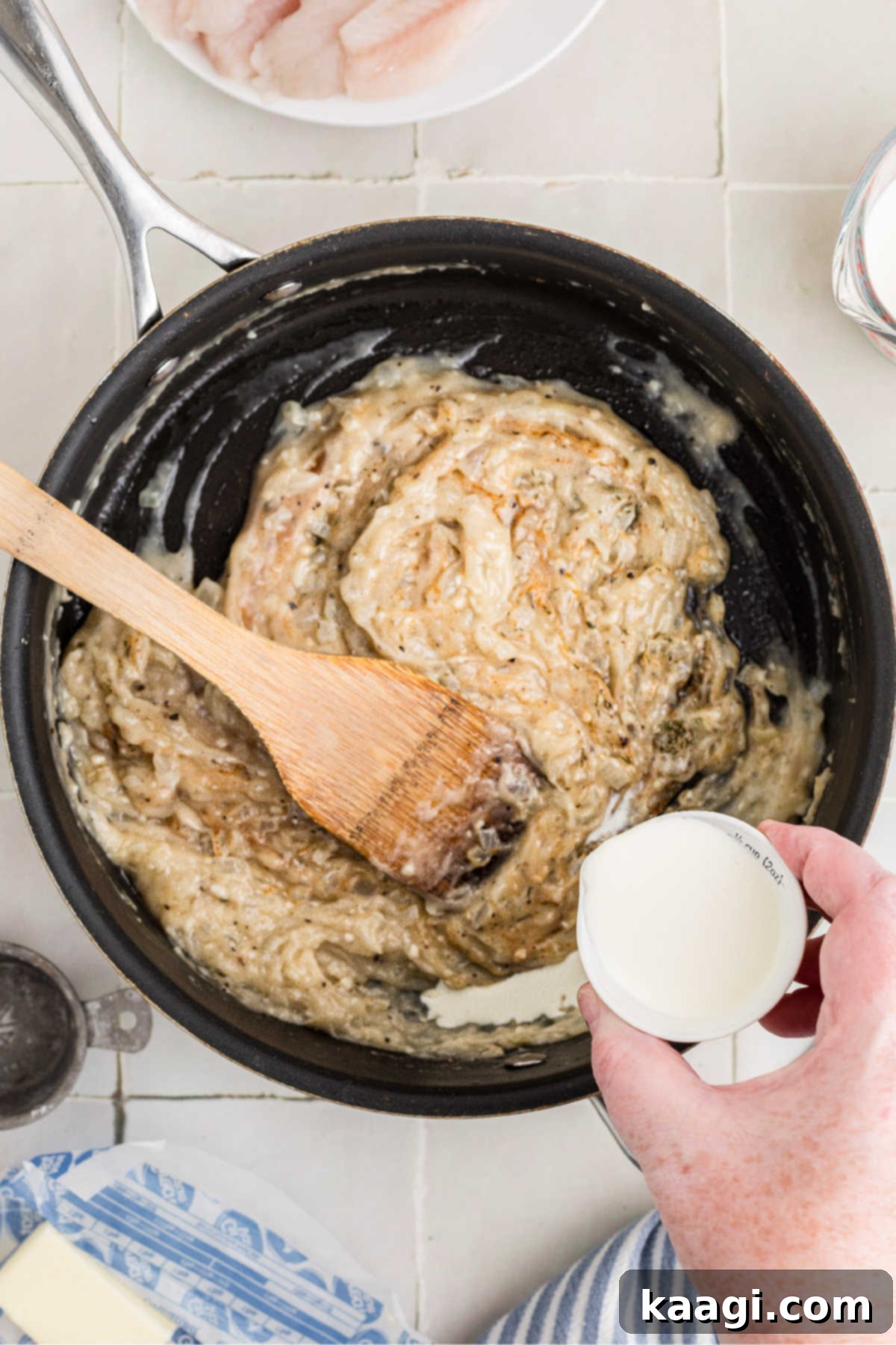A small jug of cream being poured into a skillet with onions and flour etc.