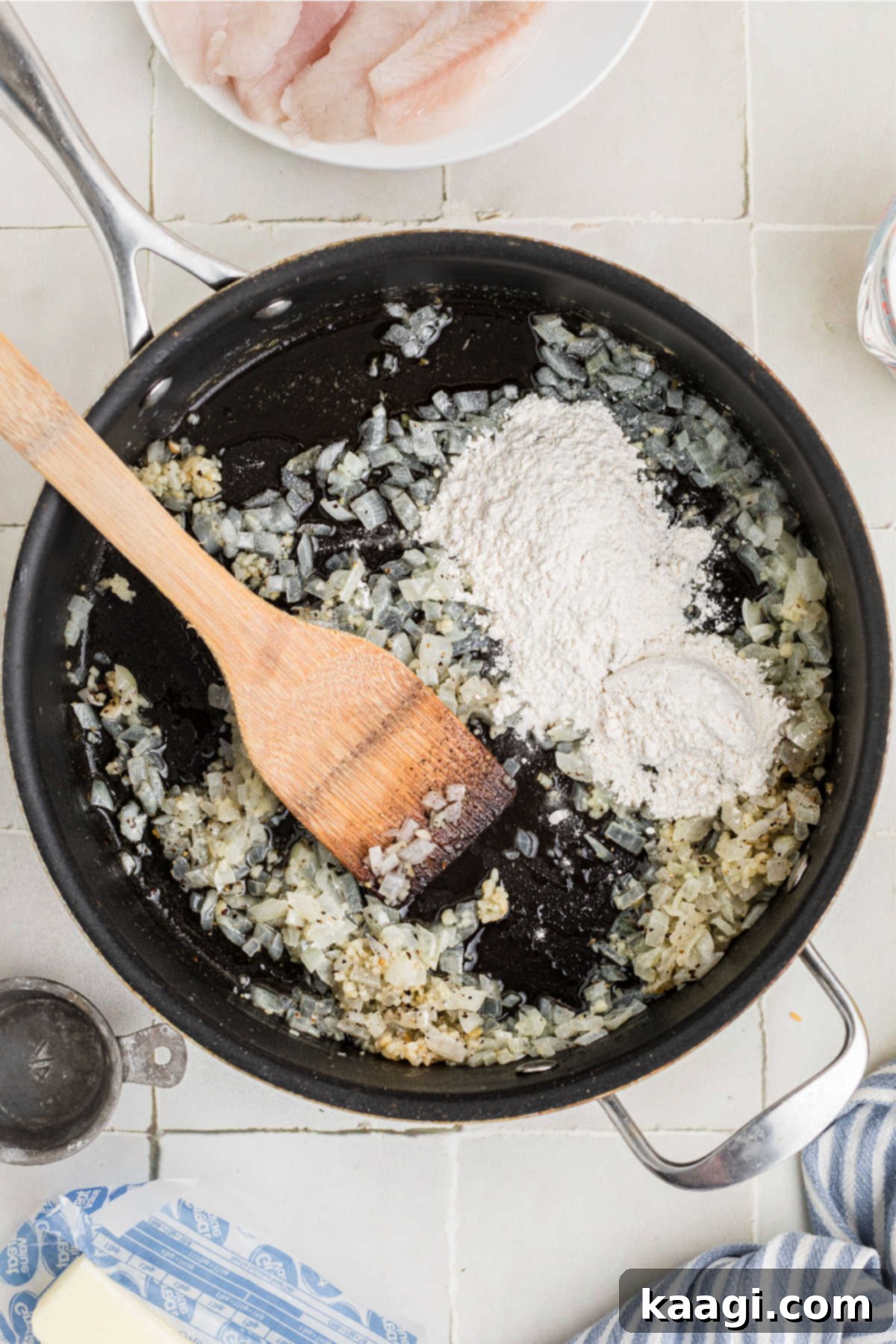Flour added to a skillet with onions and garlic.