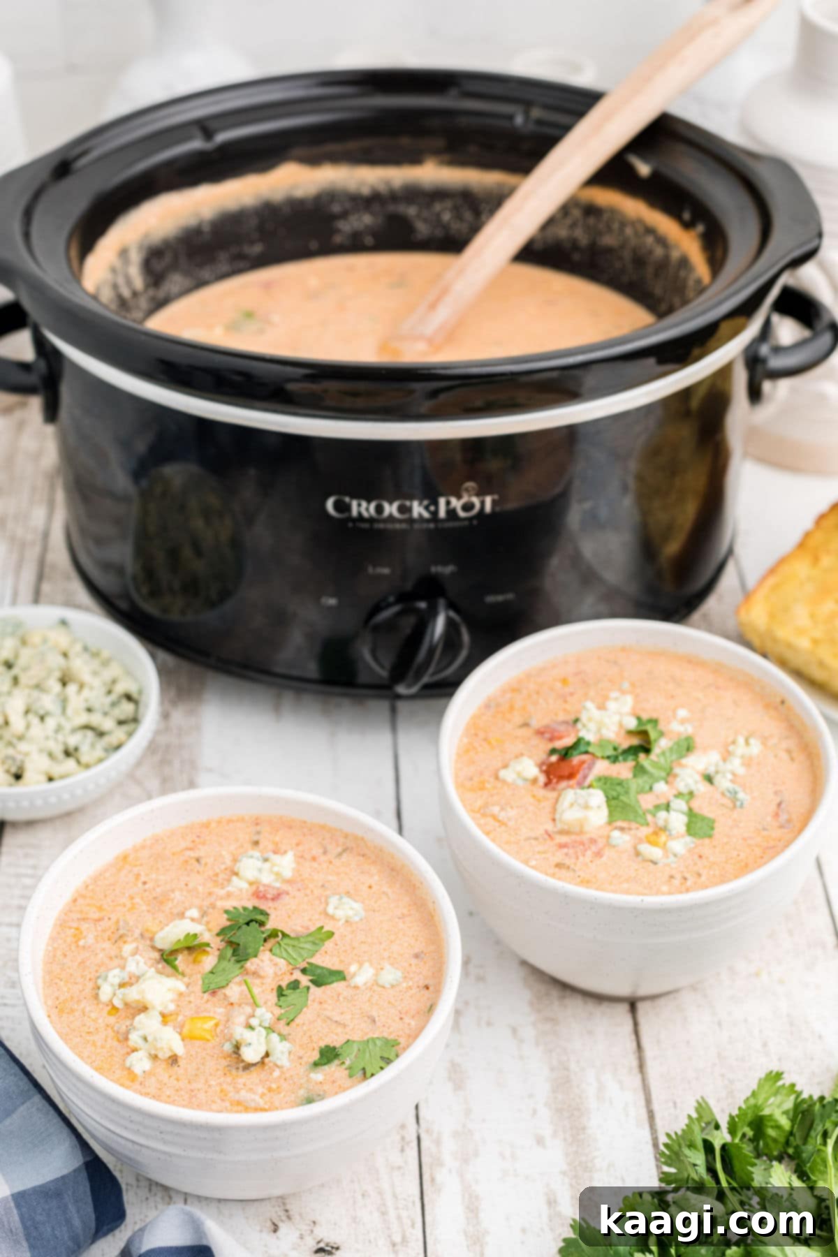 Two bowls of creamy slow cooker buffalo chicken chili in front of a slow cooker, garnished and ready to eat.