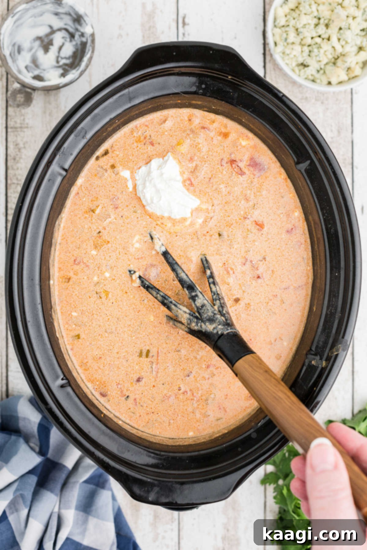 A generous dollop of sour cream being added to the finished chili in a crock pot, ready for a final stir and serving.