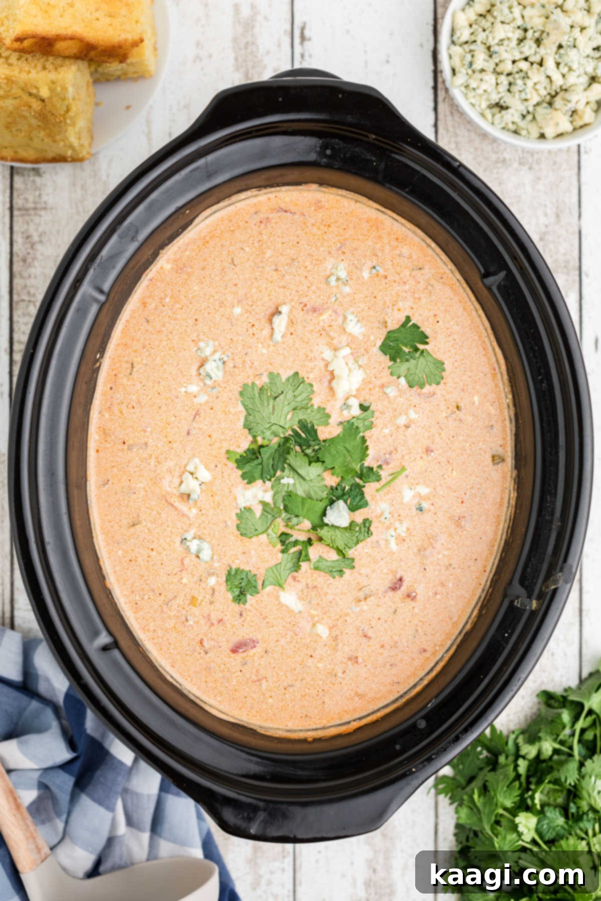An overhead shot of a slow cooker filled with buffalo chicken chili, beautifully garnished with crumbled blue cheese and fresh cilantro.